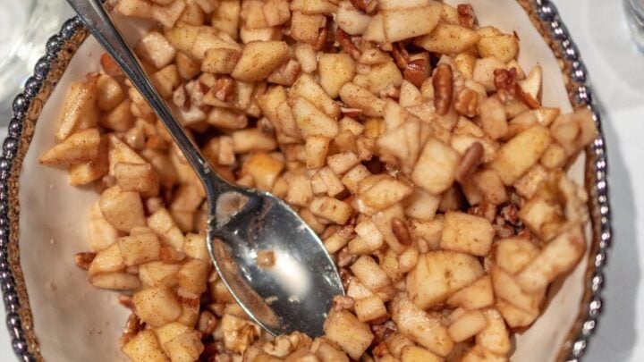 Top view of Haroset recipes of apples and pecans in an ivory colored serving dish with a silver spoon.