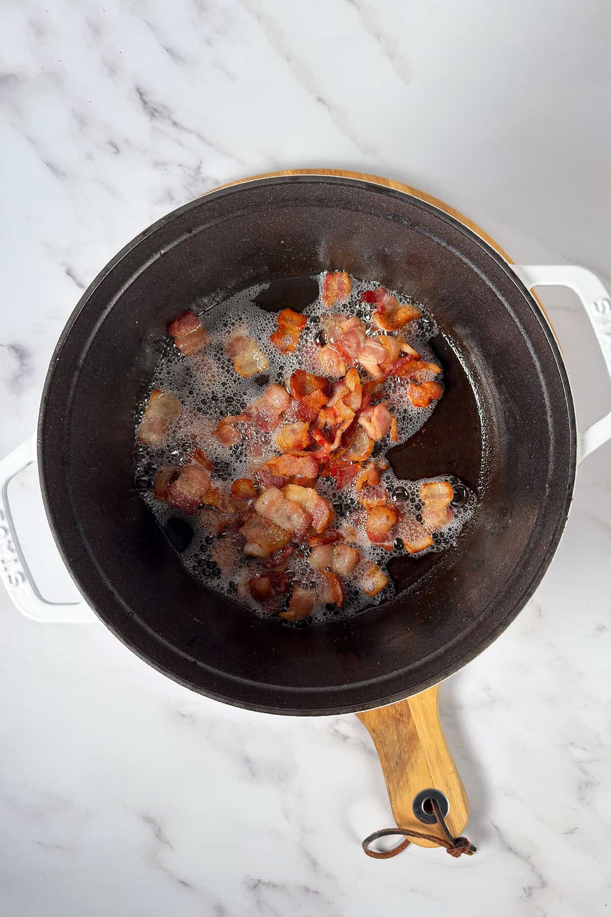 Chopped bacon pieces sizzling and browning in a black pot for Kentucky Burgoo.