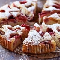 A sliced strawberry rhubarb cake dusted with powdered sugar sits on parchment paper.