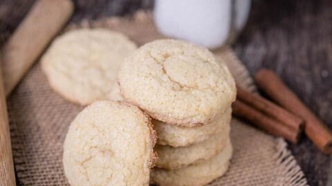 A stack of Masala Chai Cookies on a piece of burlap, with cinnamon sticks and a glass bottle of milk in the background.