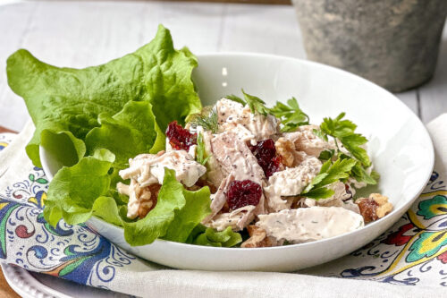 White bowl of chicken salad on lettuce leaves.