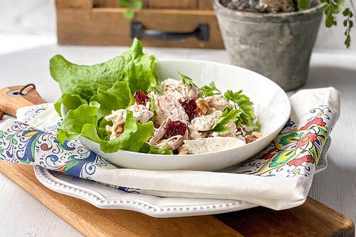 Side view of lighter Chicken Salad Lettuce Wrap in a white bowl on a wooden board.