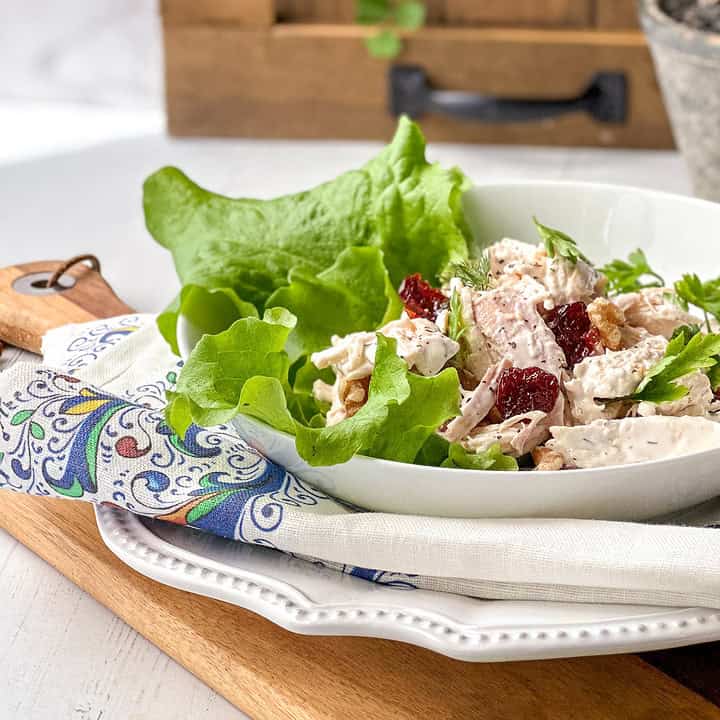 Side view of lighter Chicken Salad Lettuce Wrap in a white bowl on a wooden board.