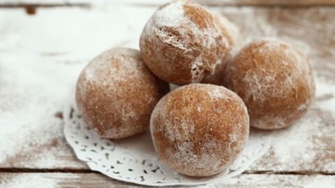 Pile of doughnut holes on a powdered sugar dusted surface.