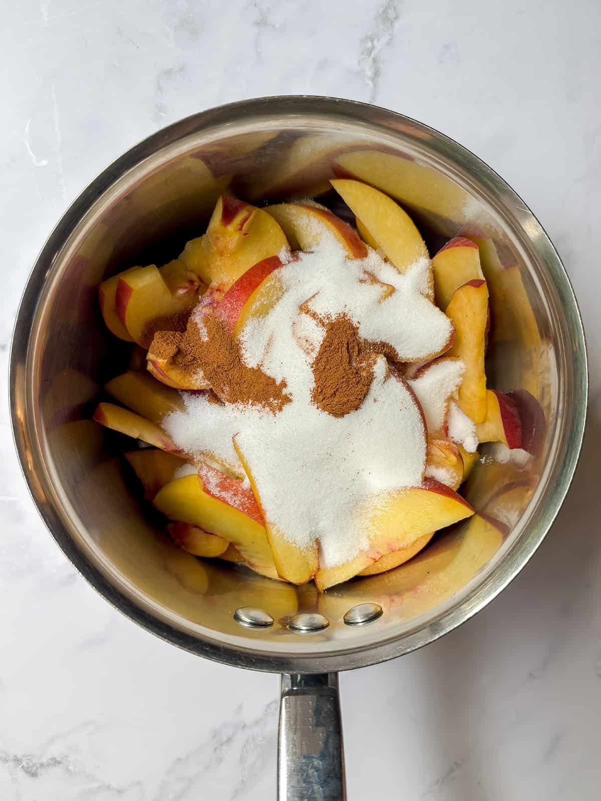 Sliced peaches with sugar, cinnamon, and salt in a saucepan.