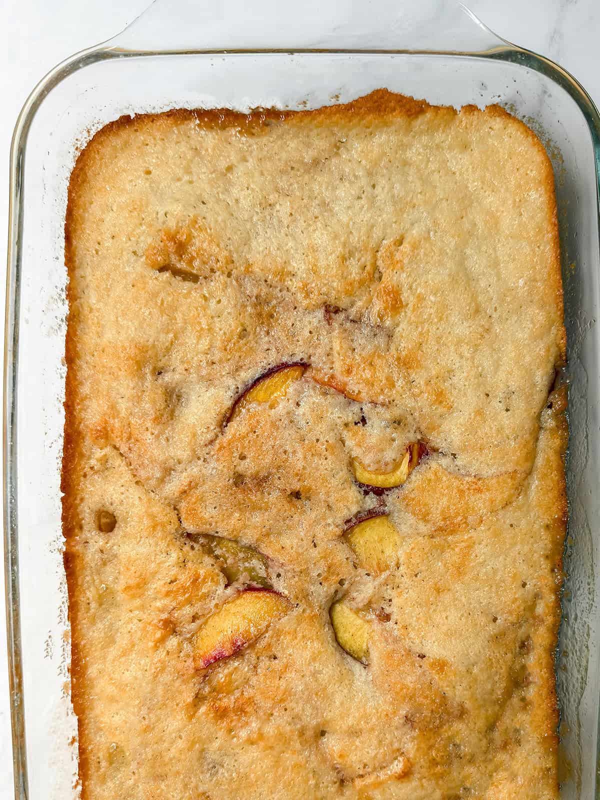 Baked peach cobbler with a golden topping and peaches showing through.
