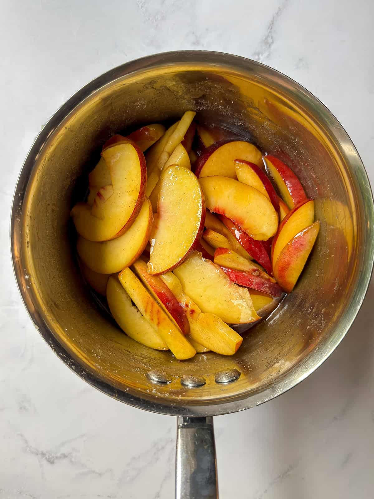 Sliced peaches and their juices after cooking briefly in a saucepan.