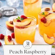 Three glasses of raspberry peach iced tea garnished with peach slices, raspberries, and mint sit on a white tray with extra fruit and a drink strainer nearby.