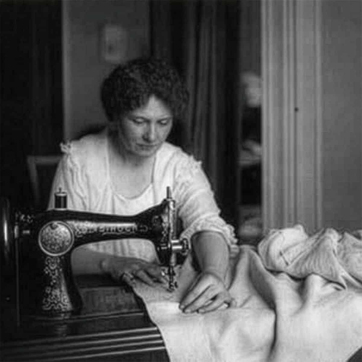 A woman operates a vintage sewing machine, skillfully guiding a flour sack under the needle in a cozy domestic setting.