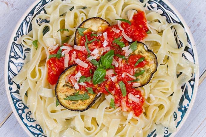 Top view of Eggplant Parmesan served over white fettuccini noodles and garnished with fresh basil and served in a blue and white bowl.