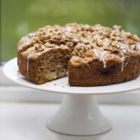 Apple cake with a slice missing on a white cake stand in the window.