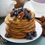 Stacked pumpkin pancakes with chocolate chips, blueberries and toasted pecans for serving.