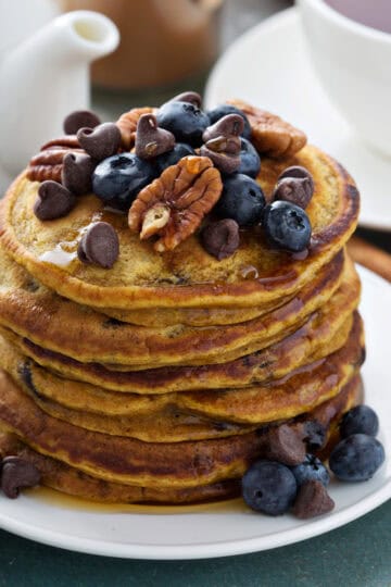 Stacked pumpkin pancakes with chocolate chips, blueberries and toasted pecans for serving.