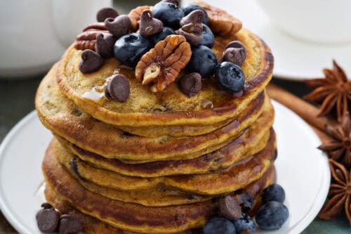 Stacked pumpkin pancakes with chocolate chips, blueberries and toasted pecans for serving.