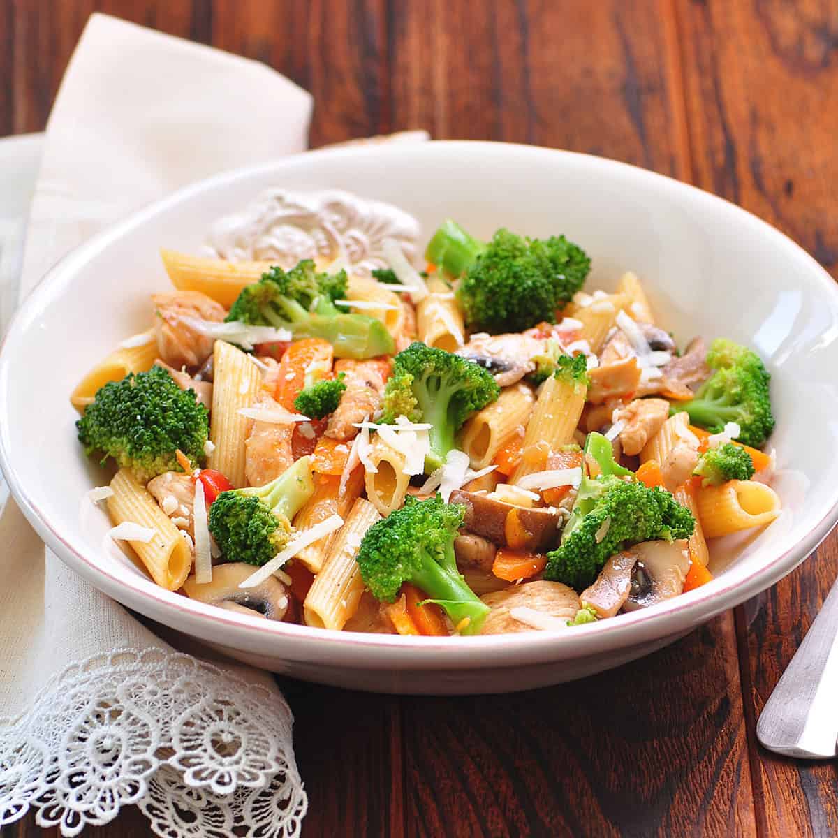 Sausage and broccoli pasta in a white bowl on a wooden surface with a serving linen nearby.