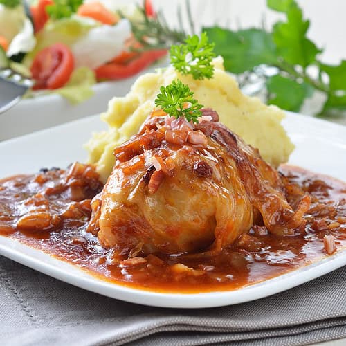 Side view of cabbage roll with sauce on a white plate with curly parsley.
