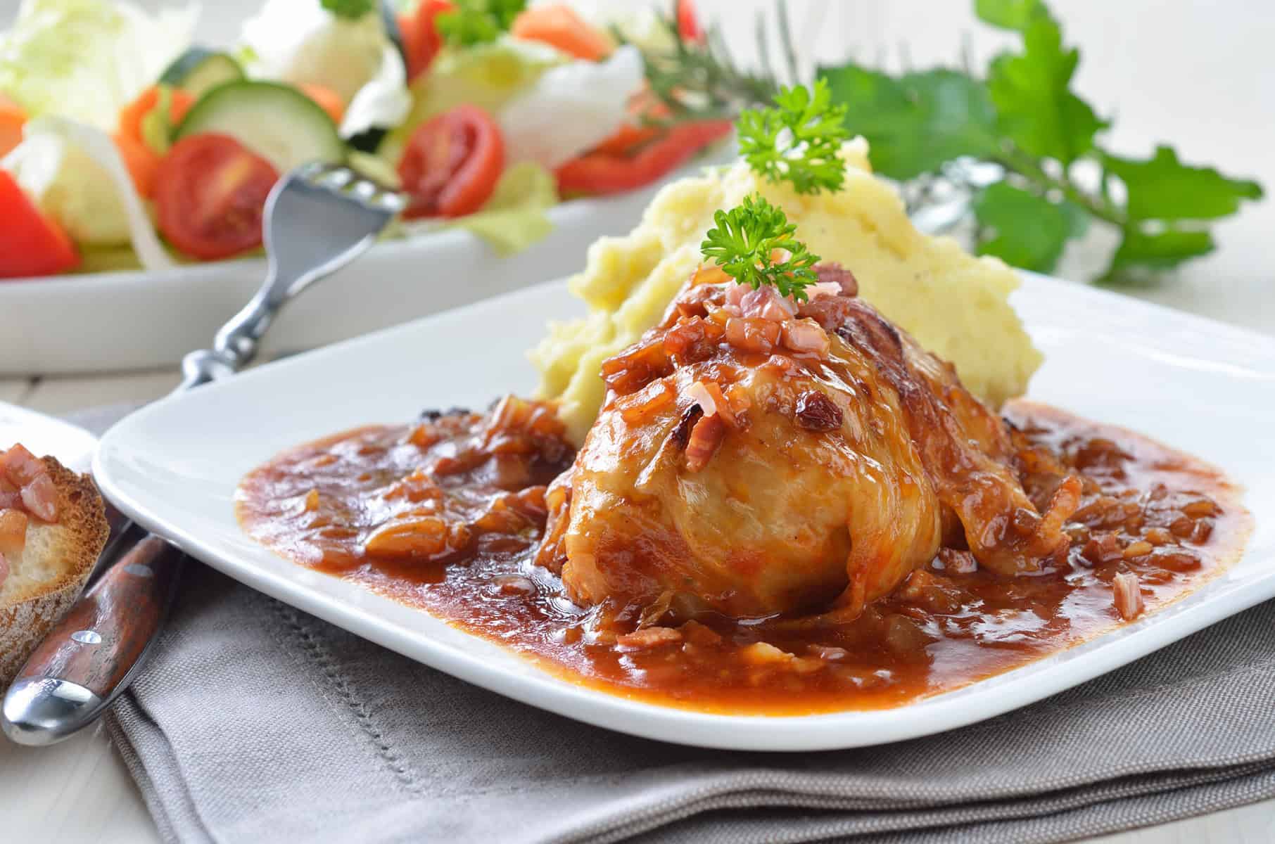 Side view of cabbage roll with sauce on a white plate with curly parsley.