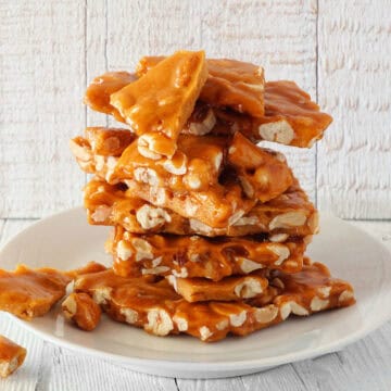 Stack of freshly made homemade peanut brittle on a white plate.