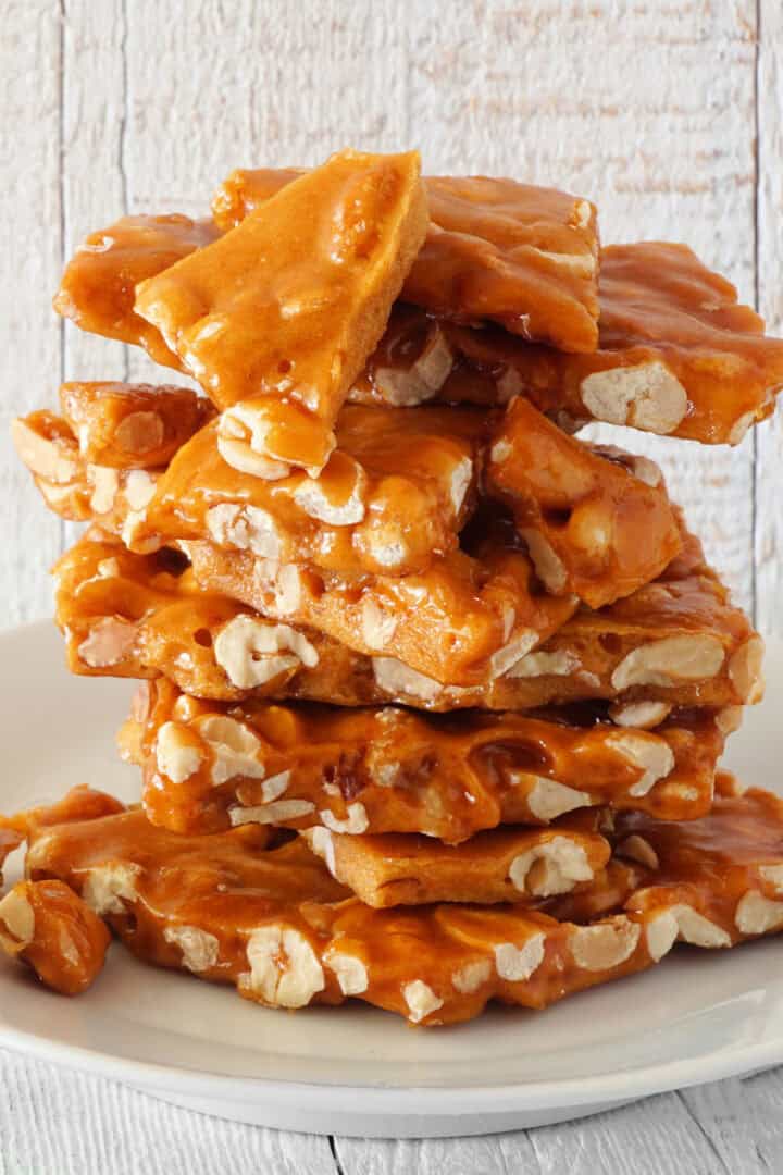 Stack of freshly made homemade peanut brittle on a white plate.