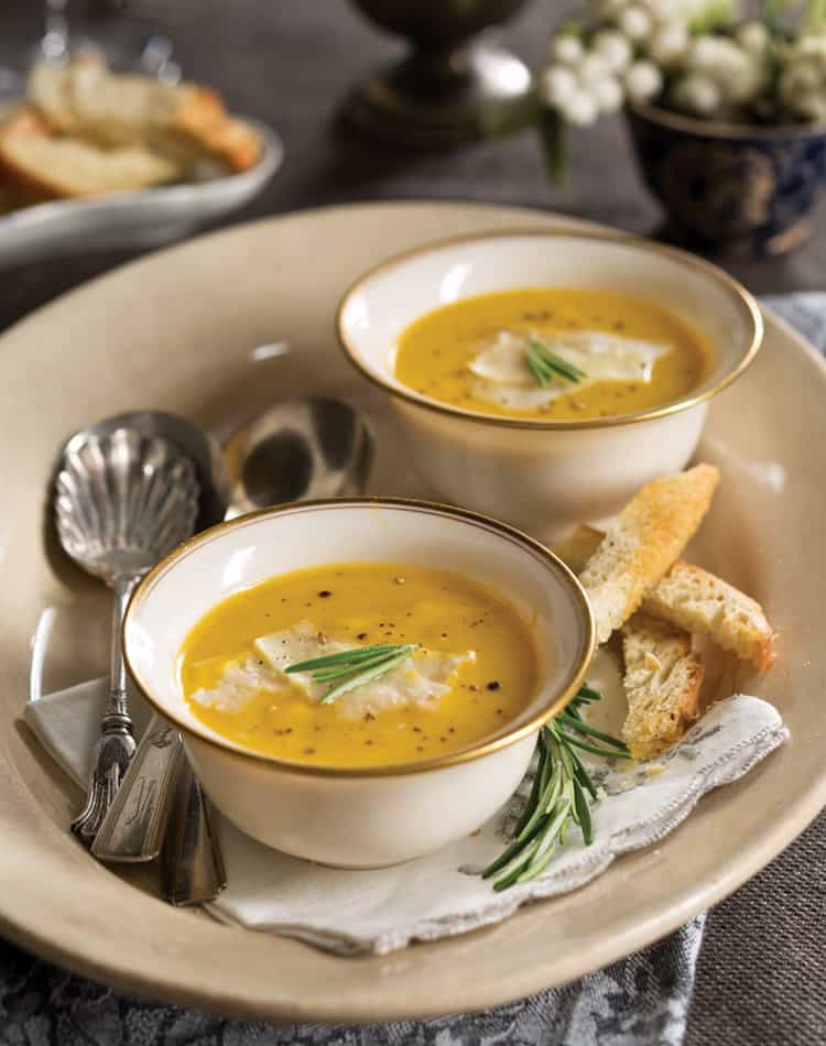 Two bowls of creamy soup garnished with herbs and cheese, served on a plate with bread slices and silverware-perfect for an Autumn Afternoon Tea.