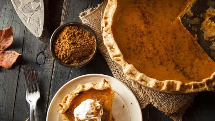 Top view of pumpkin pie with a slice sitting on a white plate. The background is a dark rustic wooden board.