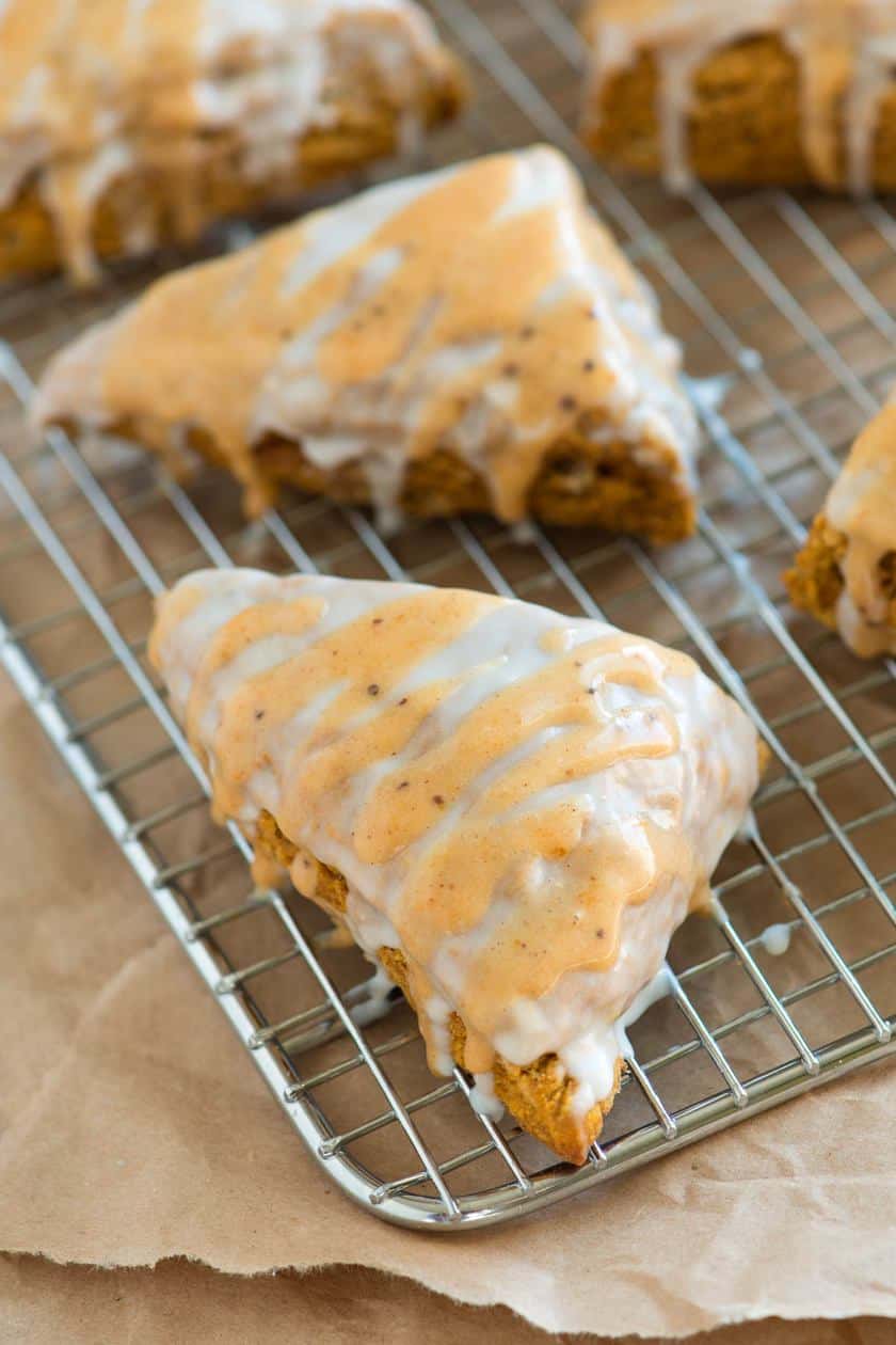 Triangular scones with white and light brown glaze are cooling on a wire rack over brown parchment paper-perfect for an Autumn Afternoon Tea treat.