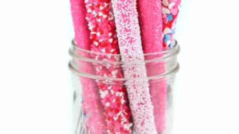 Two glass cups filled with chocolate mousse, topped with whipped cream and chocolate shavings, are placed on a tray lined with chocolate pieces—perfect as indulgent Valentine's Day treats.