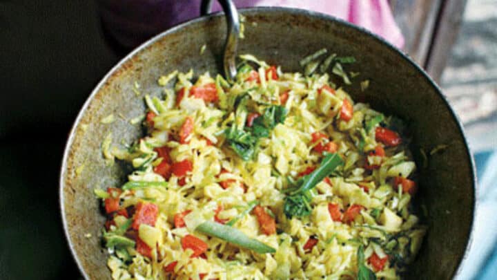 A person holds a metal pan filled with cooked yellow rice, vegetables, herbs, and tender cabbage, viewed from above—a delicious example of creative cabbage recipes.