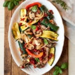 A white platter with grilled zucchini, mushrooms, onions, red bell peppers, tomato sauce, and fresh basil—perfect alongside Italian Sheet Pan Pork Chops on a rustic wooden surface.