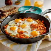 Sweet potato hash with poached eggs in a cast iron skillet with whole grain bread in the background.