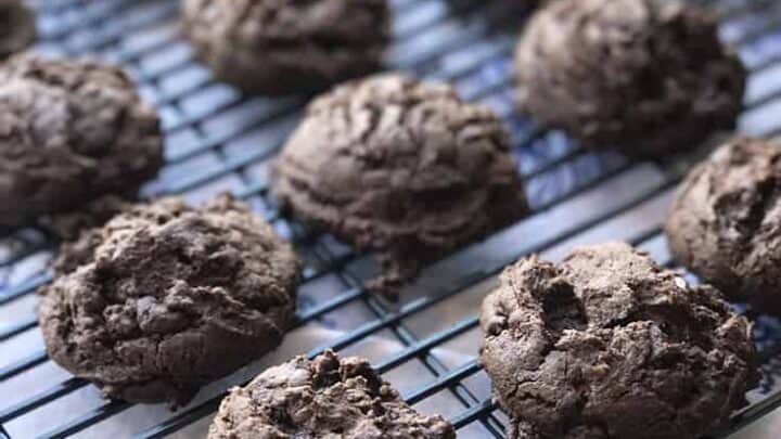 A cooling rack holds twelve freshly baked Mexican chocolate cookies. The cookies are rich in color with a soft, slightly crumbly texture. A light, patterned tablecloth is partly visible underneath the rack.