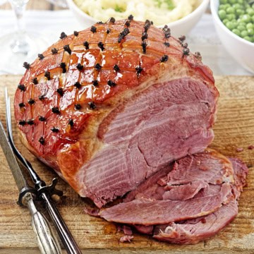 Slow cooker glazed ham studded with cloves on a carving board.