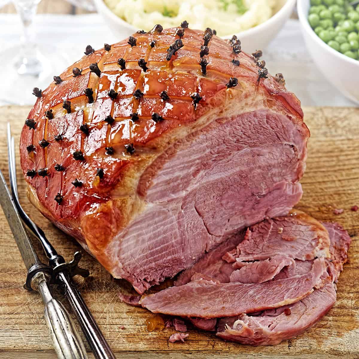 Slow cooker glazed ham studded with cloves on a carving board.