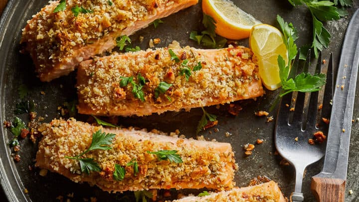 Four baked salmon fillets with a breadcrumb and herb crust are arranged on a plate, garnished with parsley and lemon wedges—perfect for healthy 20 minute dinners. A fork and knife are placed beside them, ready to enjoy.