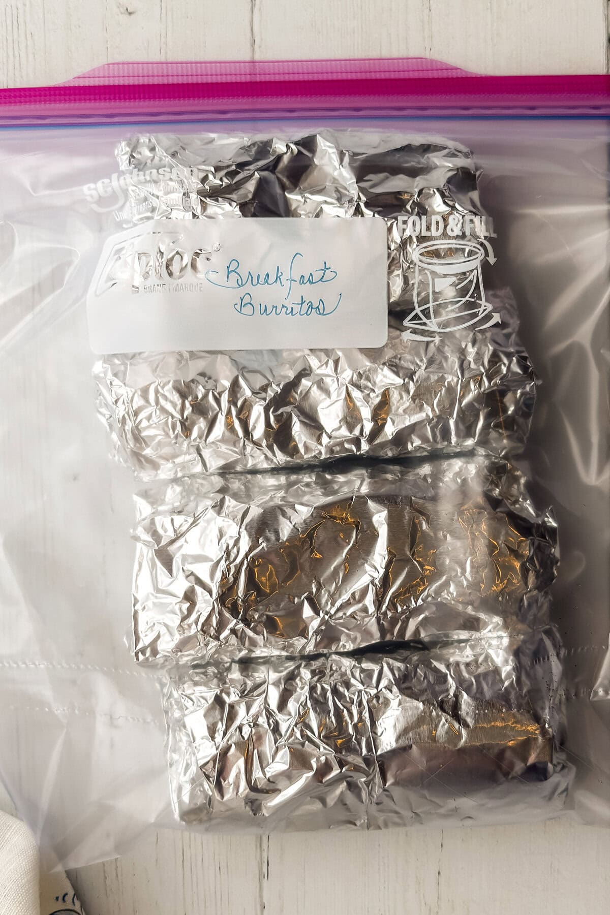 Foil-wrapped breakfast burritos stored in labeled freezer bag for meal prep.