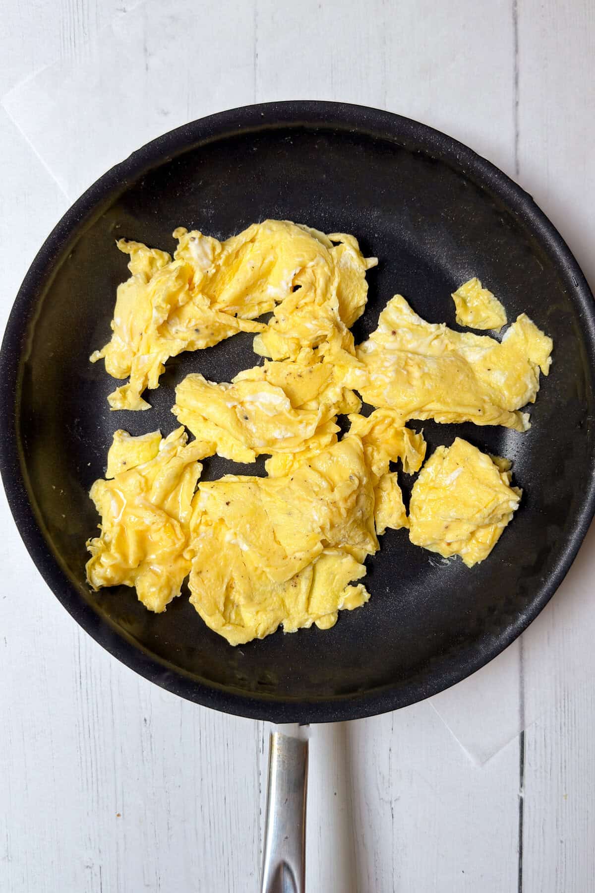 Fluffy scrambled eggs cooking in a black skillet for breakfast burritos.
