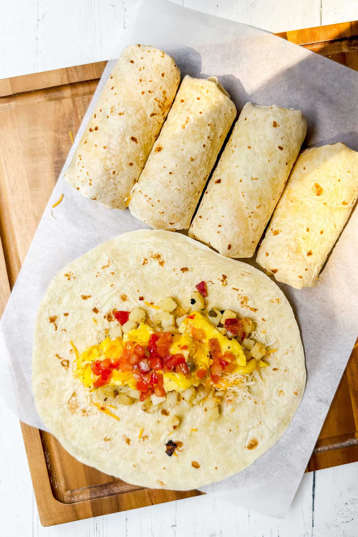 Tortilla topped with scrambled eggs, potatoes, cheese, salsa, and cilantro for breakfast burrito filling.