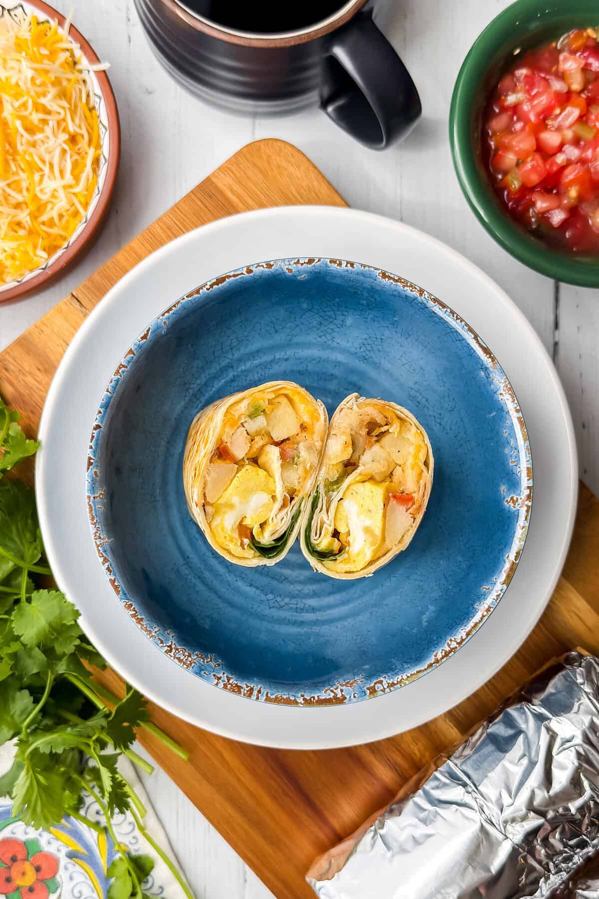 Breakfast burrito cut in half showing scrambled eggs, potatoes, cheese, and vegetables.