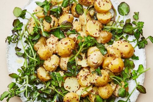 A plate of sliced baby potatoes mixed with fresh greens and coarse mustard dressing on a light surface—perfect for enjoying as one of your favorite summer side dishes.