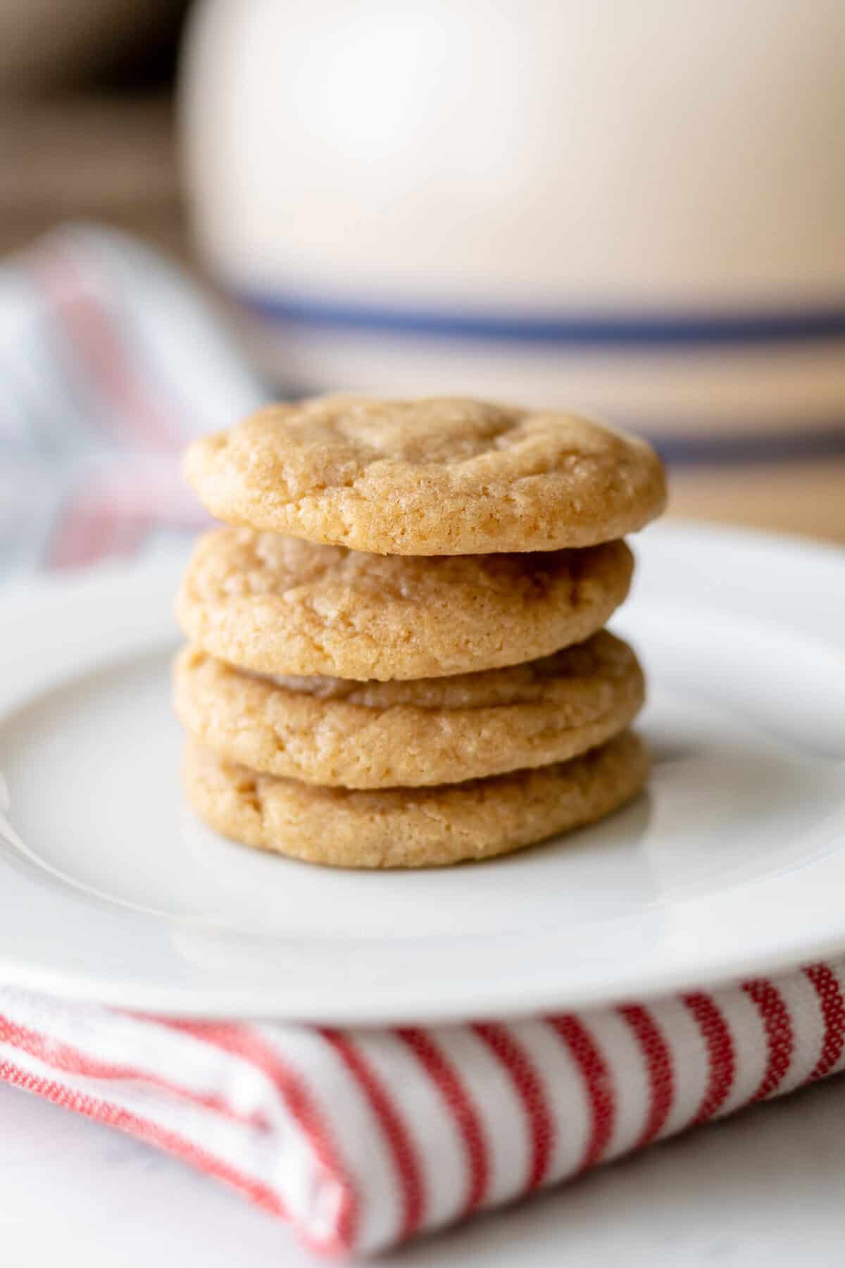 A stack of four golden-brown graham cookies sits on a white plate, which rests on a red and white striped cloth. The background is softly blurred.