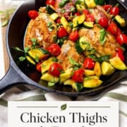 A cast iron skillet with cooked Chicken Thighs with Tomatoes and Zucchini, cherry tomatoes, and herbs on a wooden table. Text reads: “Chicken Thighs with Zucchini (One Skillet, 30 Minutes).