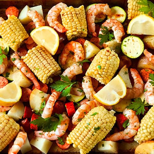 A Sheet Pan Shrimp Boil features shrimp, corn on the cob pieces, sliced sausage, potato chunks, lemon wedges, and fresh parsley, all seasoned and ready to be cooked for an easy, flavorful meal.