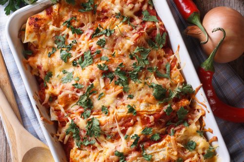 Close up of chicken enchiladas topped with melted cheese in their serving dish.