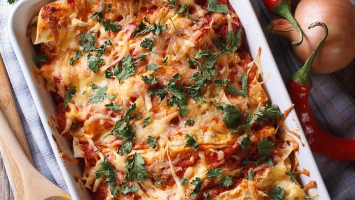 Close up of chicken enchiladas topped with melted cheese in their serving dish.
