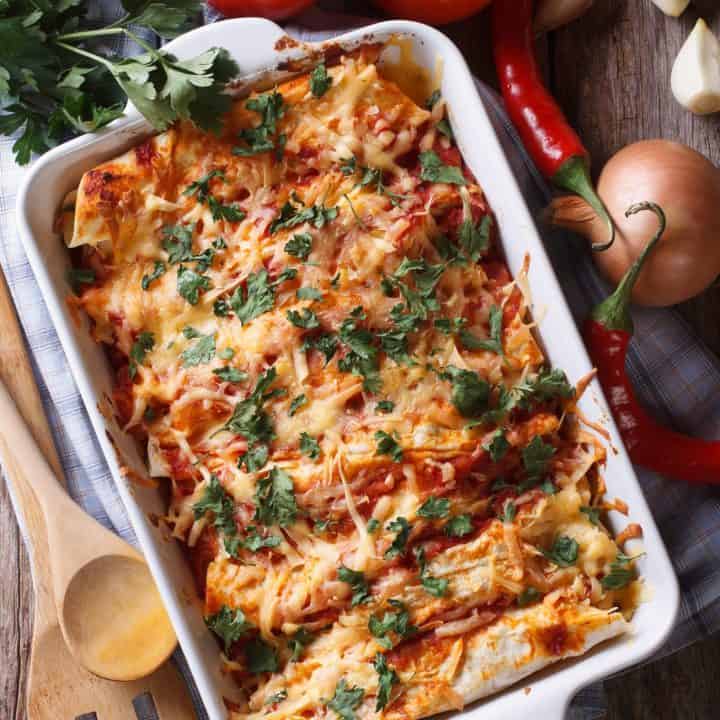 Close up of chicken enchiladas topped with melted cheese in their serving dish.