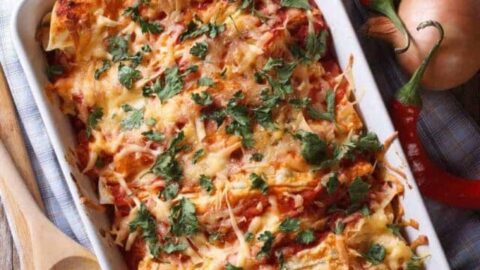 Close up of chicken enchiladas topped with melted cheese in their serving dish.