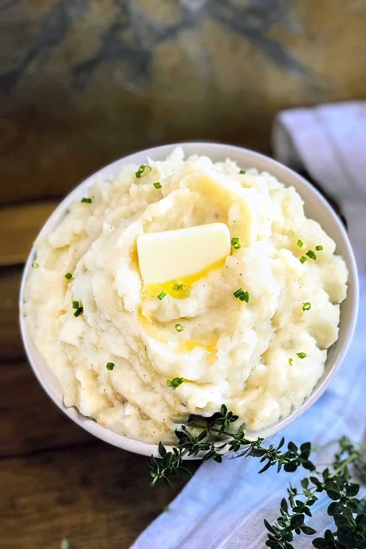 Bowl of crockpot mashed potatoes dotted with butter and snipped fresh chives.
