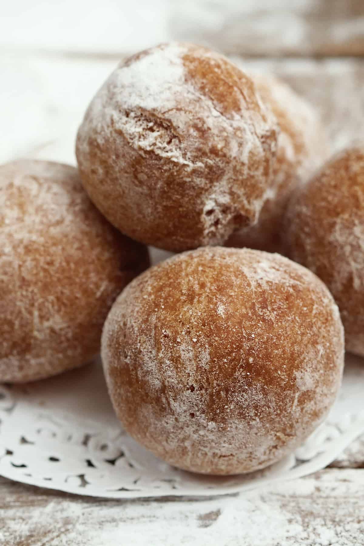 Close-up of a stack of powdered-sugar-covered baked doughnut holes on a decorative white paper doily. These golden-brown treats are nestled on a wooden surface, creating a cozy and inviting atmosphere.
