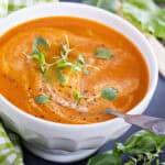 Creamy Italian inspired garden tomato soup topped with swirls of cream, microgreens and black pepper in a white bowl.