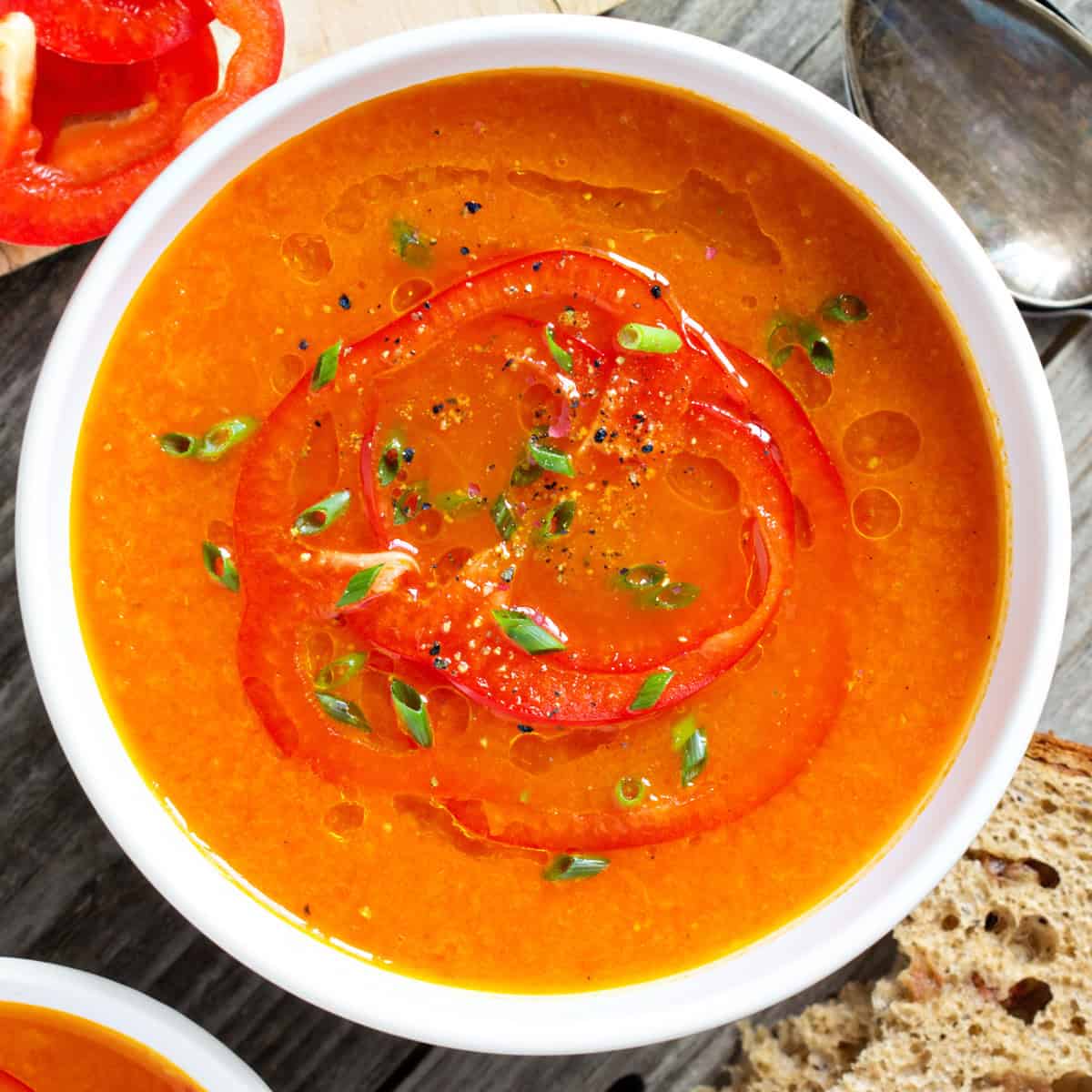 Roasted tomato and red pepper soup garnished with fresh chopped green onions and chives in a white bowl.